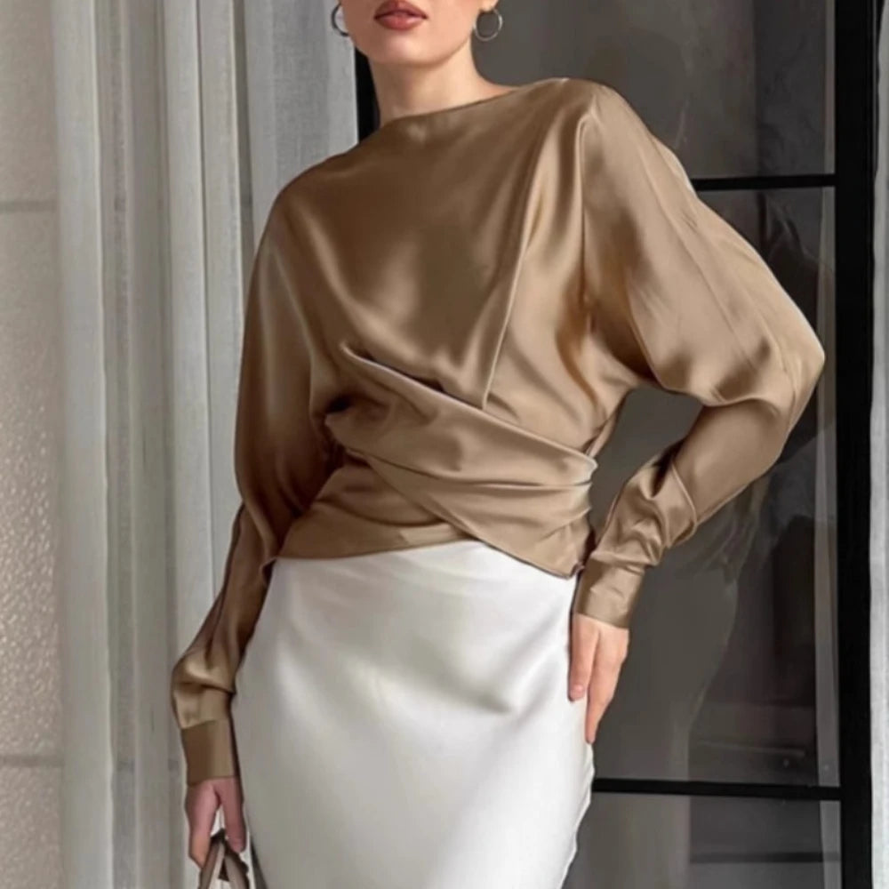Woman wearing a beige satin top and white skirt indoors.