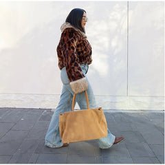 Person wearing a leopard print coat and holding a yellow bag on a city street.