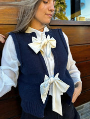 Woman wearing a navy blue knitted vest with white bows, standing against a wooden background.