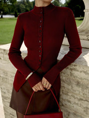 Person wearing a red ribbed sweater and brown skirt with a matching handbag, standing outdoors.