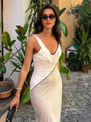Woman in a white dress with black trim standing outdoors with plants around