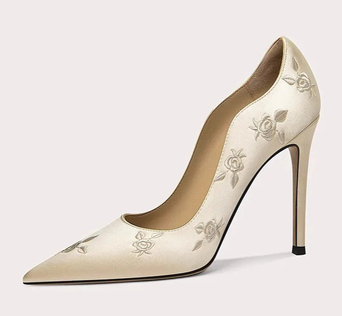Beige high-heeled shoe with floral embroidery on a light gray background
