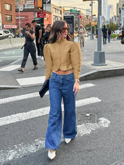 Woman in mustard jacket and blue jeans crossing a city street.