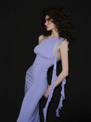 Woman wearing a lavender one-shoulder gown with ruffle details on a black background