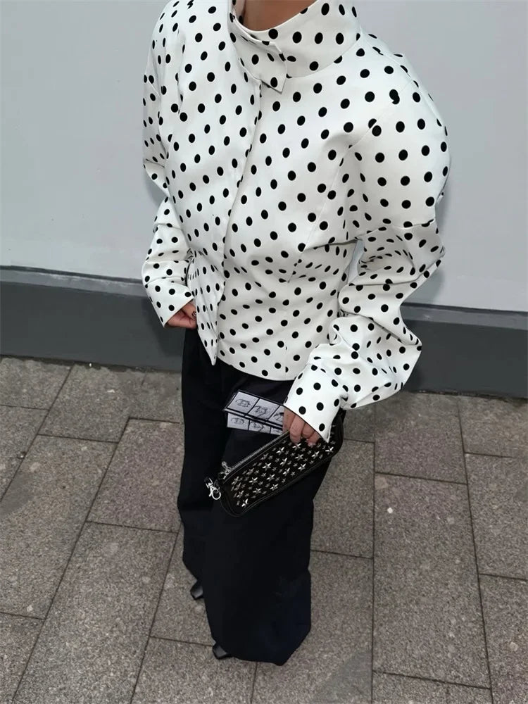Person wearing a white blouse with black polka dots and holding a patterned handbag on a tiled floor.