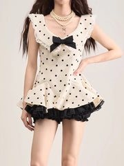 Woman wearing a polka dot dress with a black bow tie on a plain background