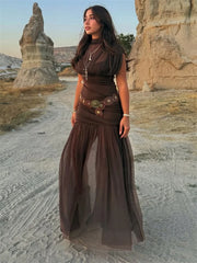 Woman in a brown dress standing in a desert landscape with rock formations.