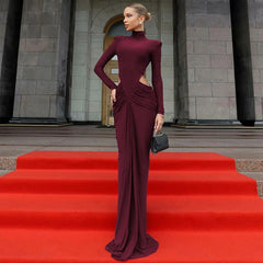 Woman in a burgundy evening gown standing on a red carpet in front of a stone building.