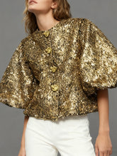 Gold sequin cape worn by a model against a gray background
