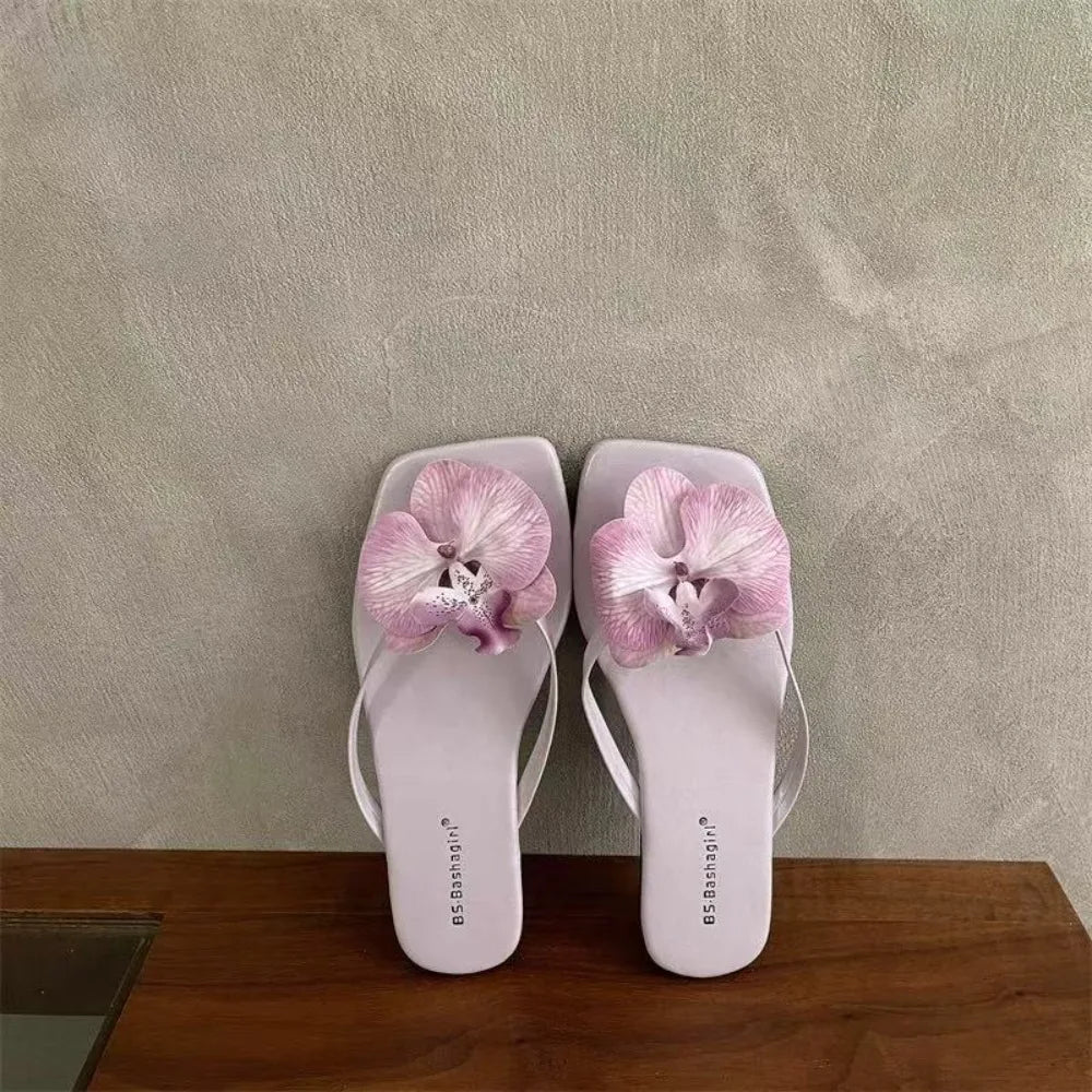 White flip-flops with pink floral decorations on a wooden surface and gray wall background