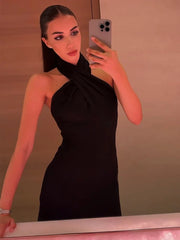 Woman taking a mirror selfie wearing a black halter neck dress.