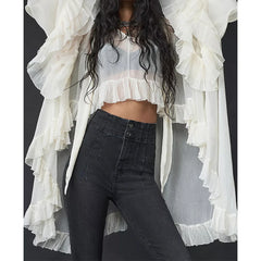 Person wearing a white ruffled top and black pants with a plain background