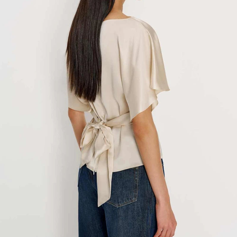 Woman wearing a beige top with a tie detail and blue jeans on a white background