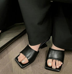 Person wearing black open-toe high-heeled sandals on a wooden floor.