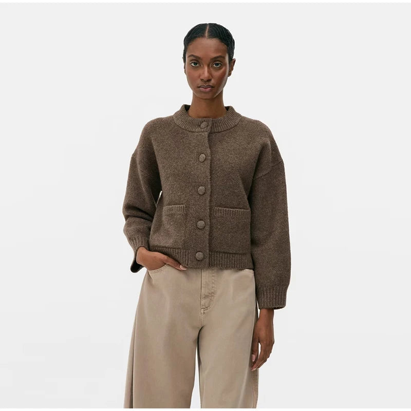 Woman wearing a kase knitted cardigan and beige pants on a white background