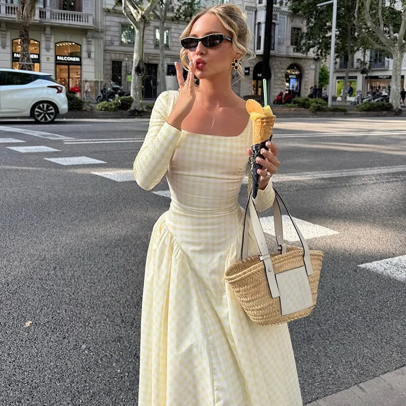 Woman in a yellow dress holding an ice cream cone on a city street.