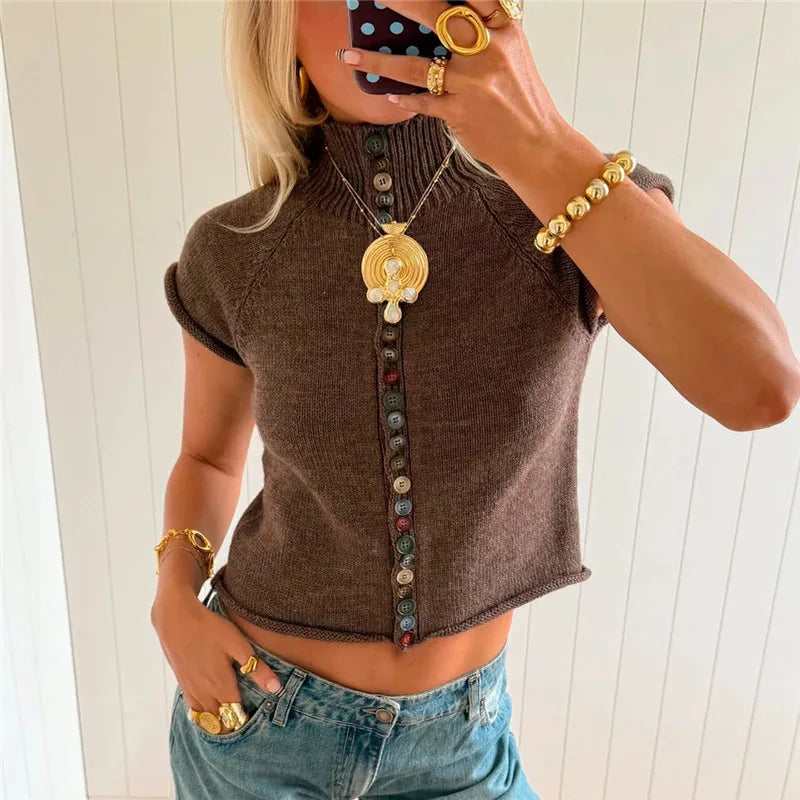 Person wearing a brown short-sleeve top with decorative buttons and blue jeans, holding a phone with a polka dot case.