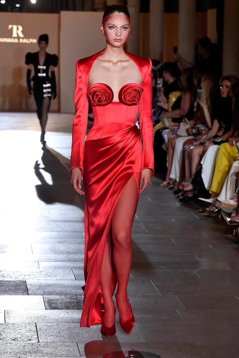 Model wearing a red dress with floral details on a runway