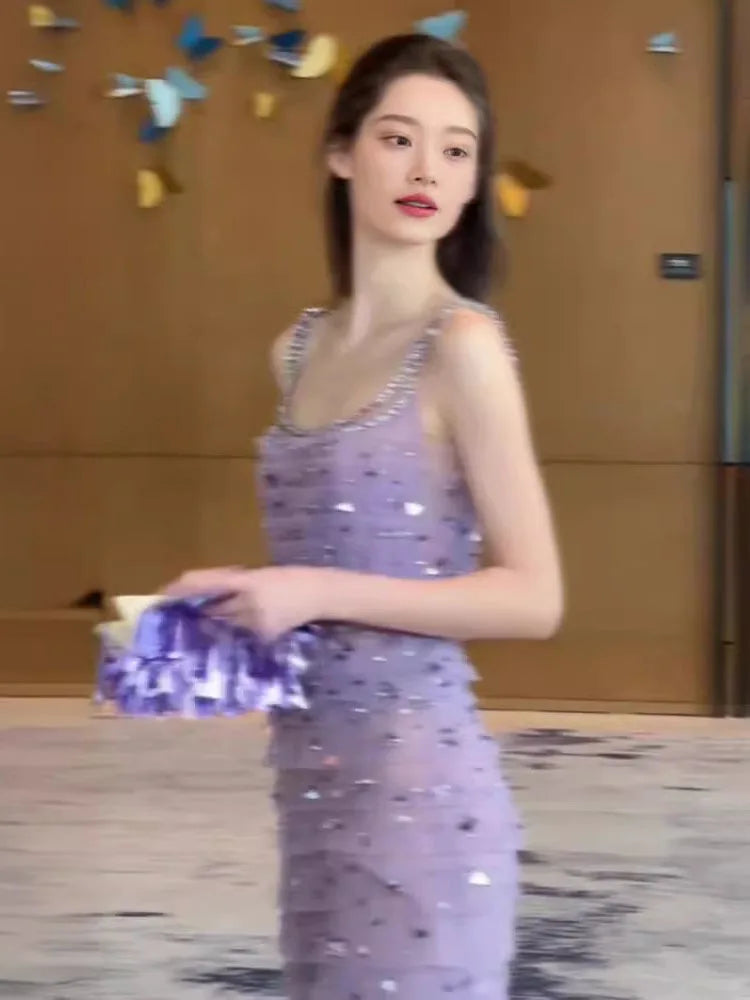 Woman in a purple sequined dress holding a blue clutch in an indoor setting