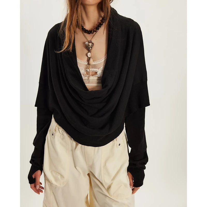 Person wearing a black draped top over a sheer beige garment with white pants on a light background