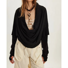 Person wearing a black draped top over a sheer beige garment with white pants on a light background