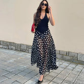 Model wearing a black polka dot maxi dress with a V-neck and sleeveless design.