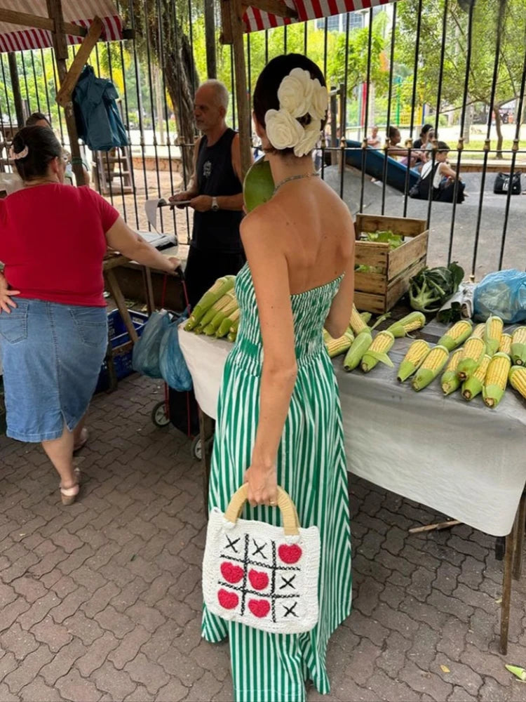 Woman in a green dress with a white bag featuring red apples and black X's at an outdoor market.