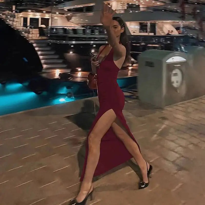 Person walking at night in a burgundy halter neck maxi dress with a thigh split