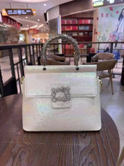 White ostrich embossed top handle bag with crystal clasp and textured handle, placed on a wooden table.