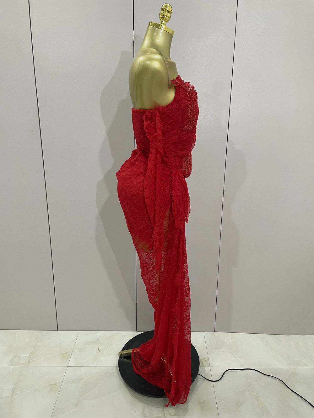 Red lace dress on a gold mannequin against a white wall.