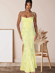 Woman wearing a bright yellow lace dress standing in a room with a wooden floor and a chair.