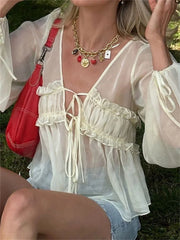 Person wearing a white blouse with ruffles and a red handbag, sitting outdoors.
