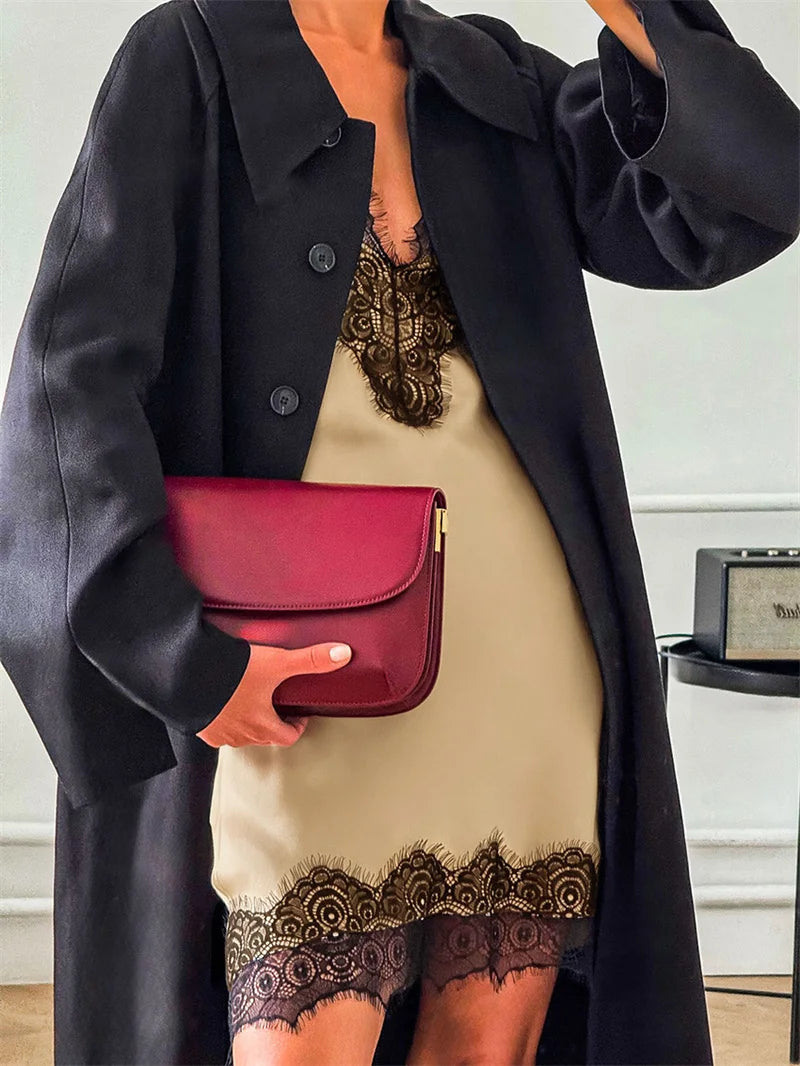 Person wearing a black coat and beige dress with lace details, holding a red handbag.
