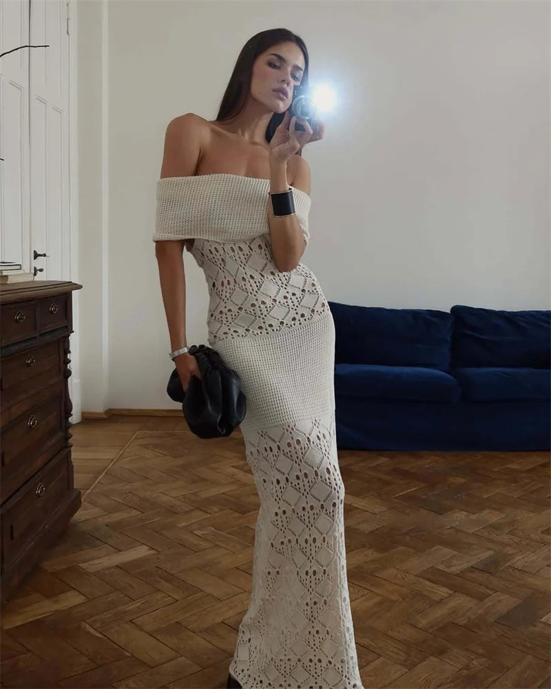 Woman in a white off-shoulder dress taking a mirror selfie in a room with wooden flooring and a blue couch.