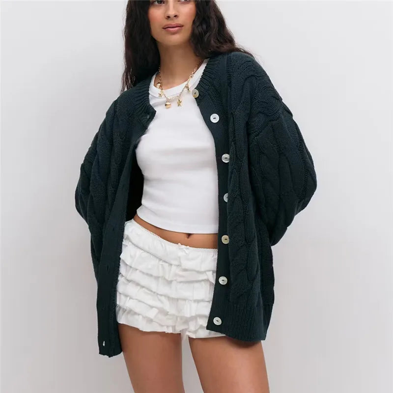 Woman wearing a dark green cardigan over a white top and skirt on a plain background