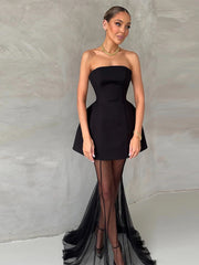 Woman wearing a black strapless dress with a high slit on a neutral background