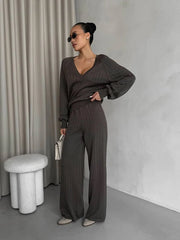 Woman in a dark gray outfit standing in a minimalistic room with a curtain and stool.