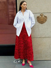 Woman wearing a white blouse and red skirt standing in front of a building entrance.