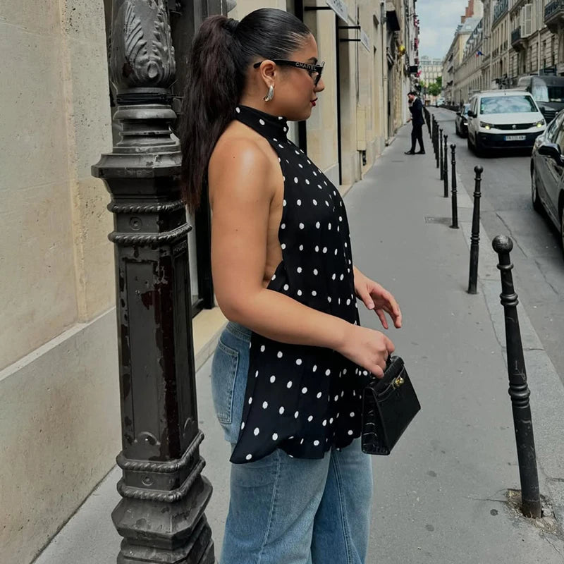 Woman in a polka dot top and jeans standing on a city street.