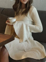 Woman in a beige dress holding a white cup, sitting on a couch.