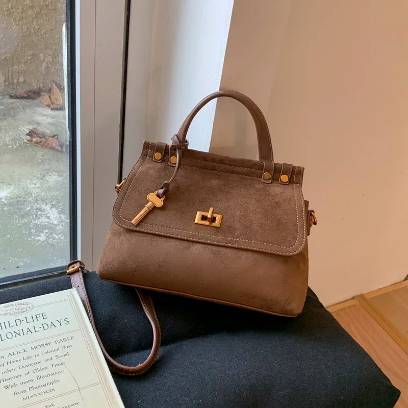 Brown handbag with gold accents on a black surface near a window