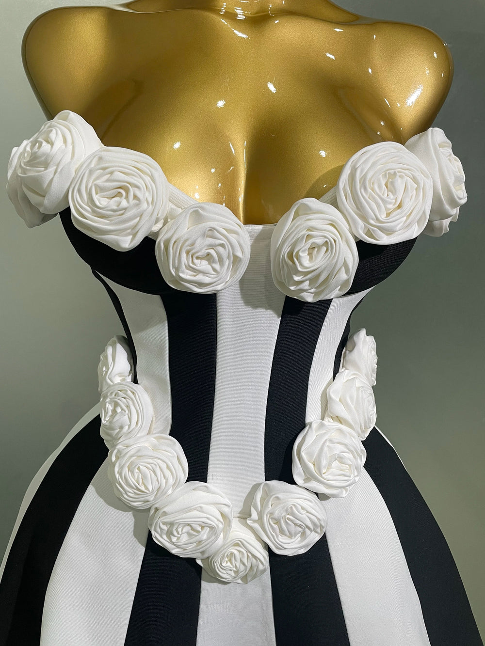 Mannequin torso with gold top and black and white striped skirt, adorned with white floral decorations.