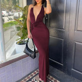 Woman in a burgundy dress holding a black handbag, standing in front of a building entrance.