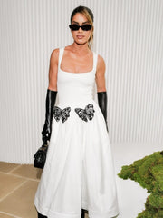Woman in a white dress with black butterfly accents and black gloves against a white background
