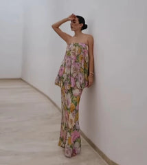 A woman wearing a floral strapless dress is standing against a white wall.