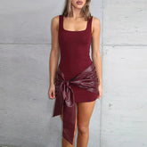 Woman wearing a burgundy dress with a large bow detail against a gray concrete wall.