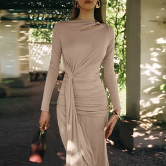 Woman wearing a beige long-sleeve dress with a knot detail, standing outdoors.