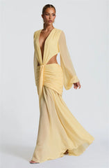 Woman wearing a yellow evening gown with a plunging neckline and long sleeves on a white background