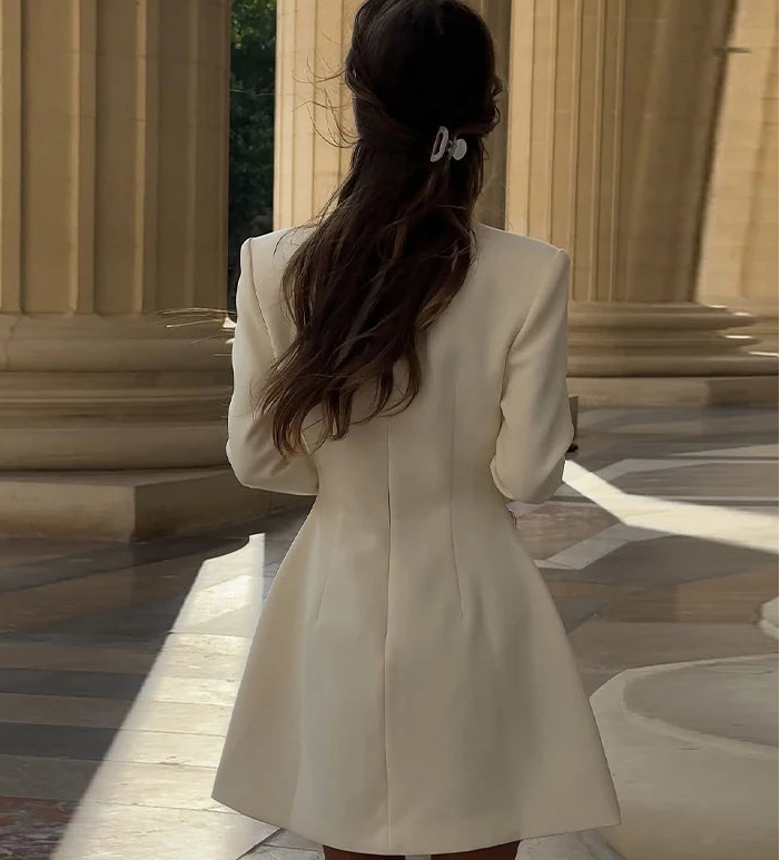Woman in a beige coat standing in front of classical architecture