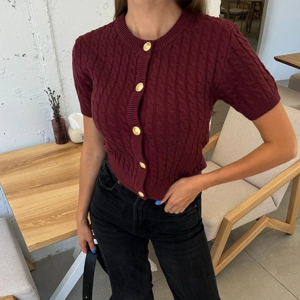 Person wearing a maroon cable knit cardigan with gold buttons in an indoor setting.